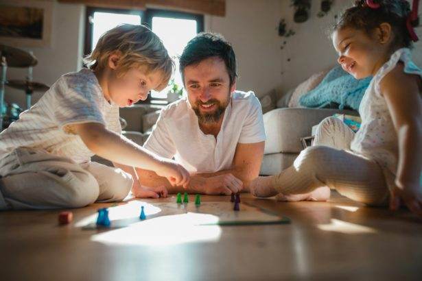 Mature father with two small children resting indoors at home, playing board games